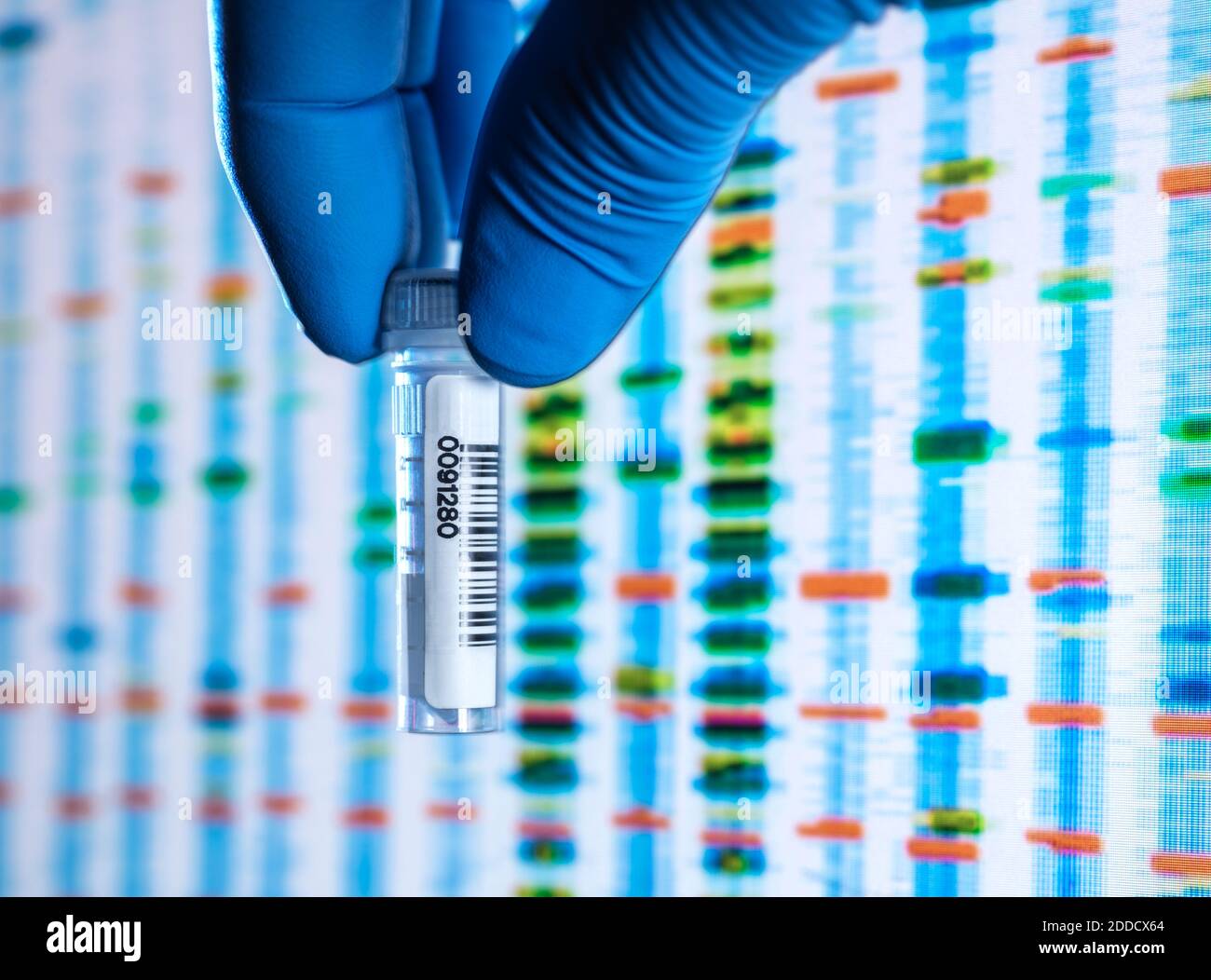 Scientists hand in latex glove holding vial containing sample with DNA results on screen in background Stock Photo