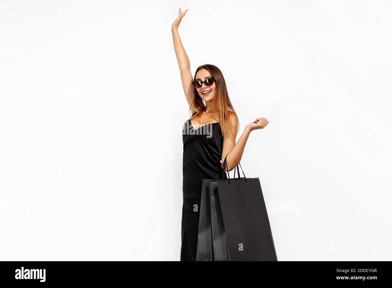 Excited young woman in black dress and sunglasses, with black shopping bags on white background, shopping concept, Black Friday Stock Photo