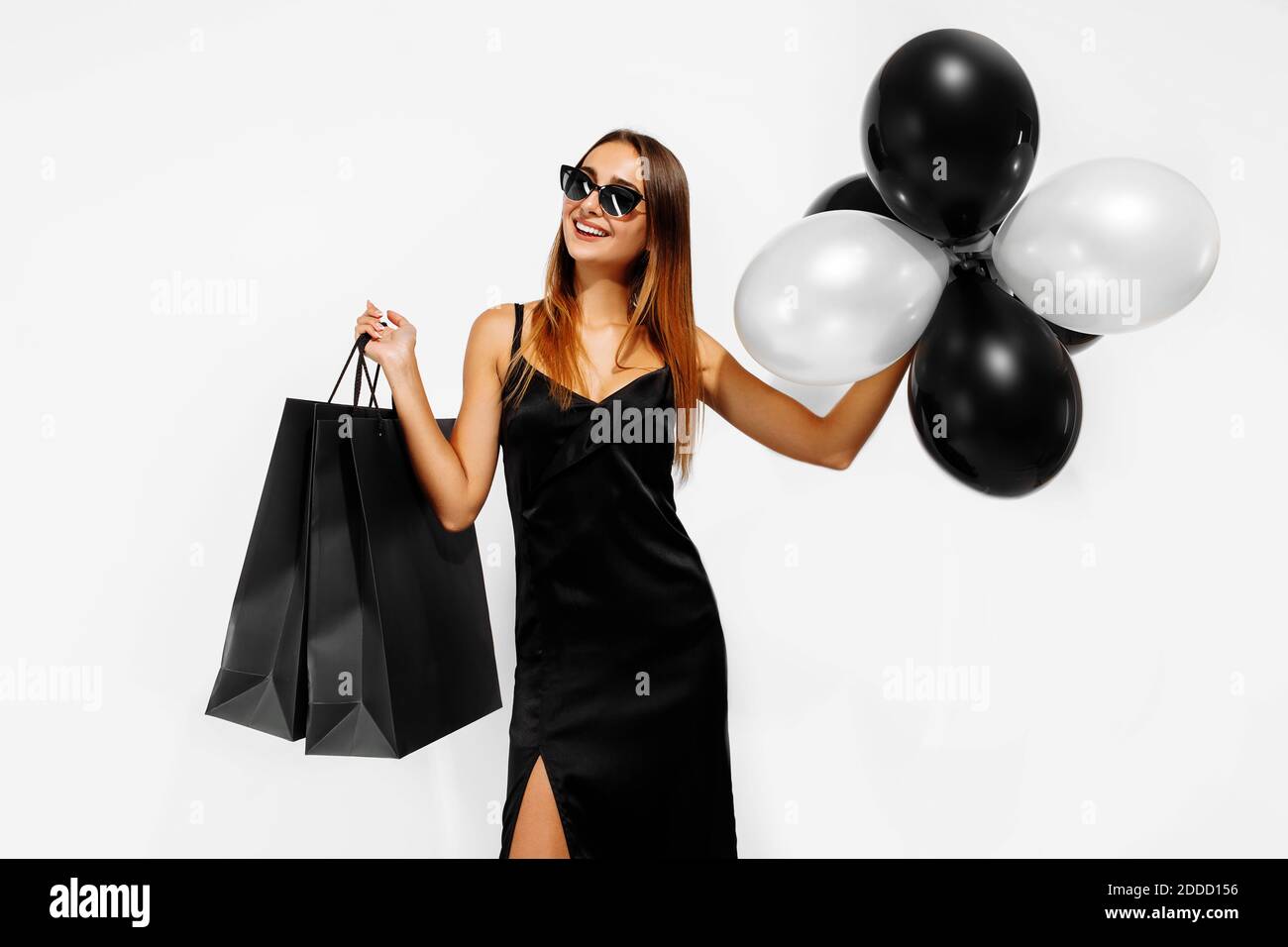 Excited young woman in black dress, with balloons and shopping bags, on white background, Concept of sale, shopping, Black Friday Stock Photo