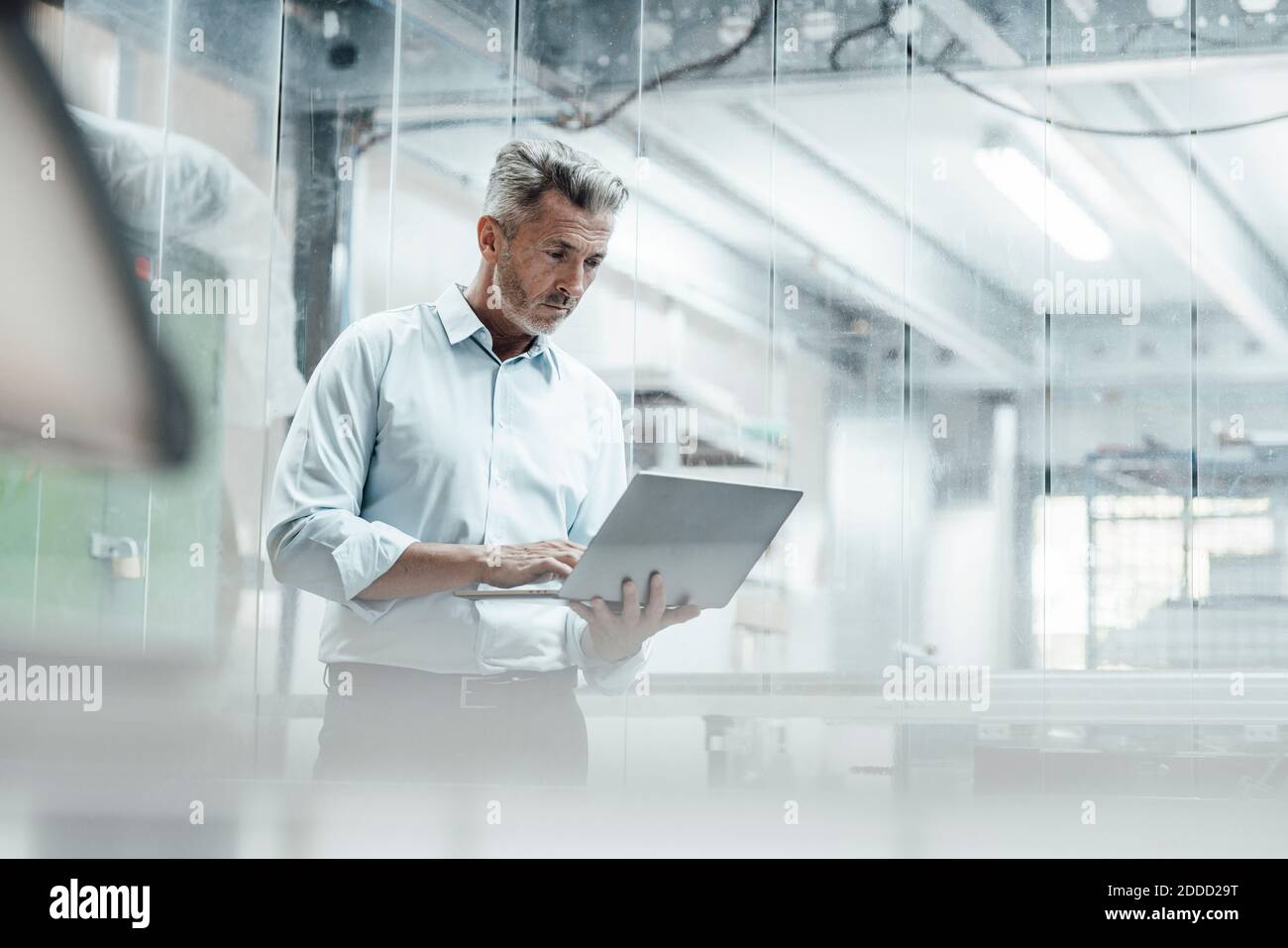 Thoughtful male engineer using laptop while standing in industry Stock Photo