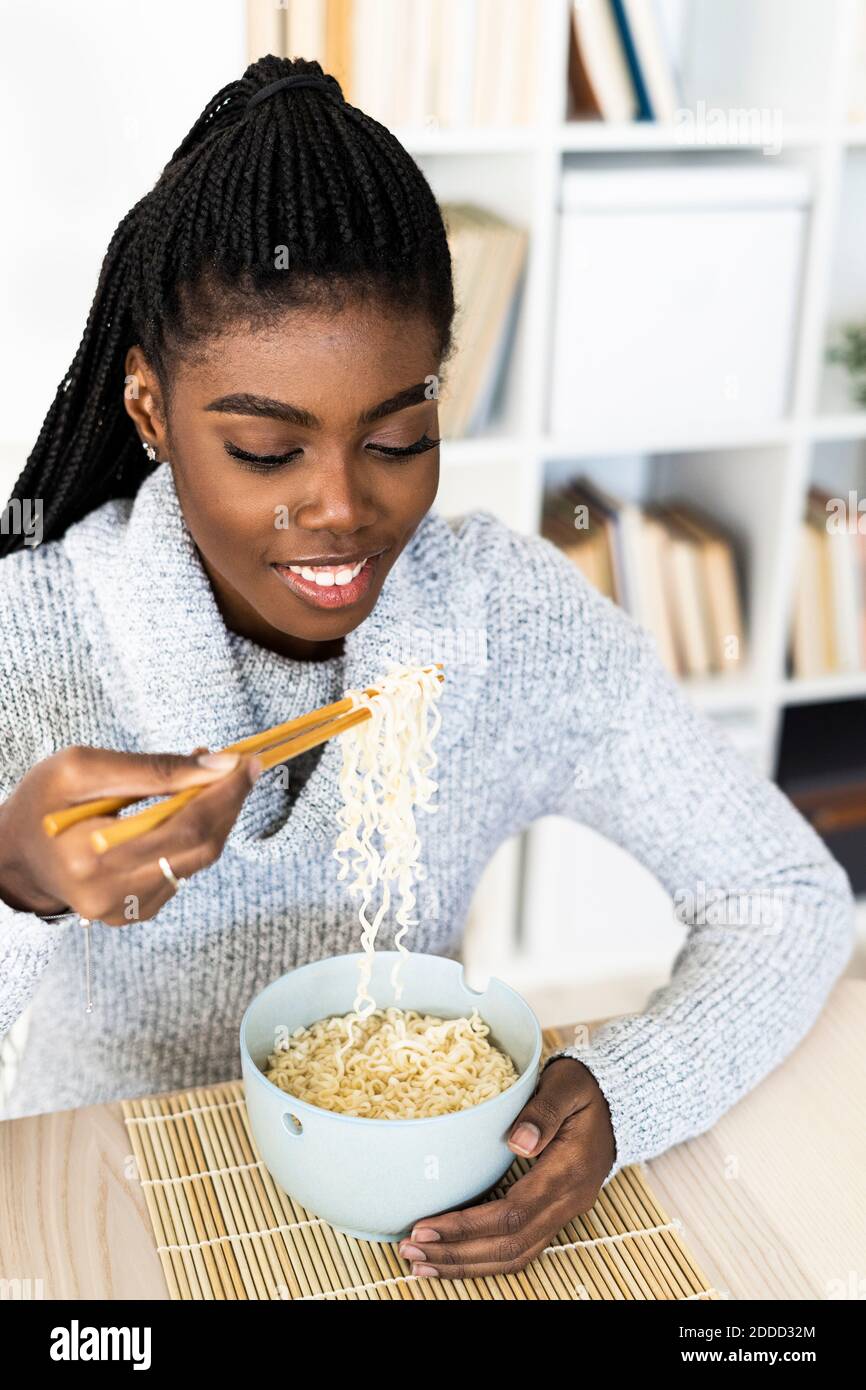 Woman eating noodles with chopsticks while sitting at home Stock Photo