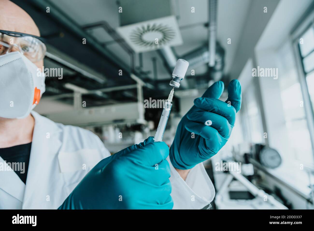 Scientist with protective face mask and eyeglasses holding injected vaccine while standing at laboratory Stock Photo