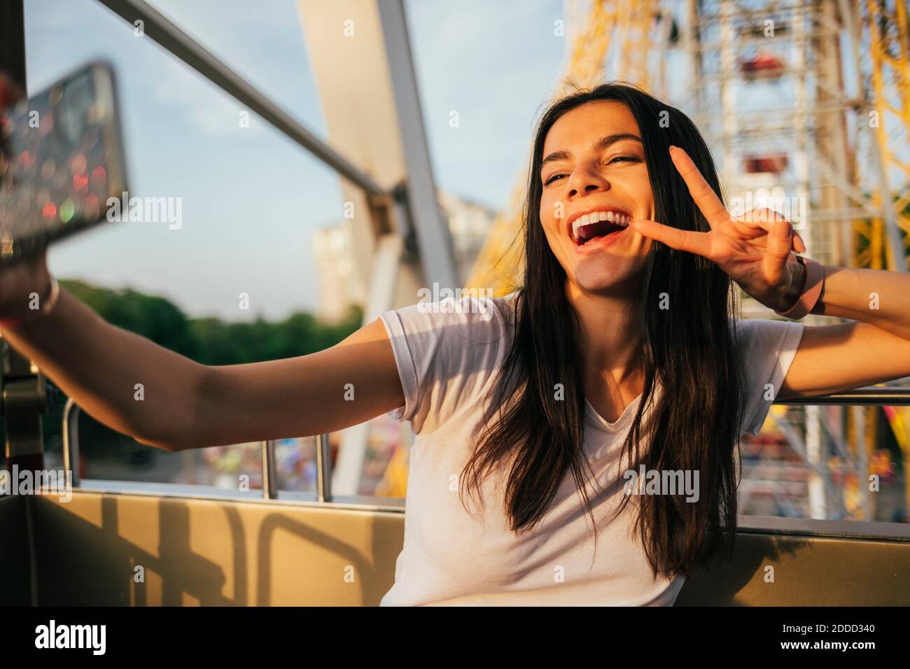 Cheerful woman on Ferris wheel using mobile phone while taking selfie at amusement park Stock Photo