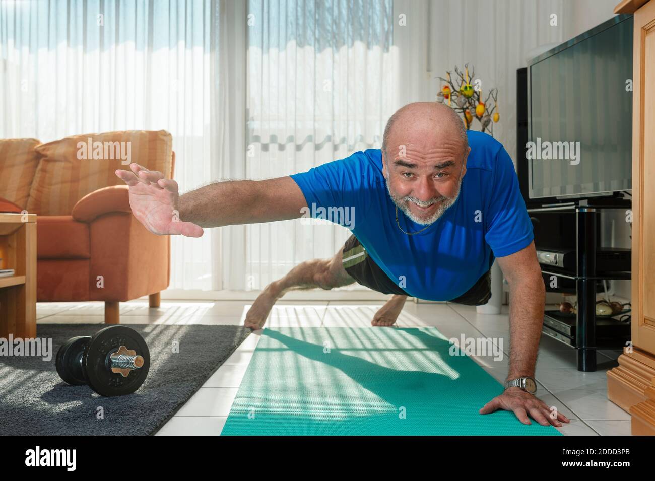 Happy senior man doing one-handed pushup at home Stock Photo