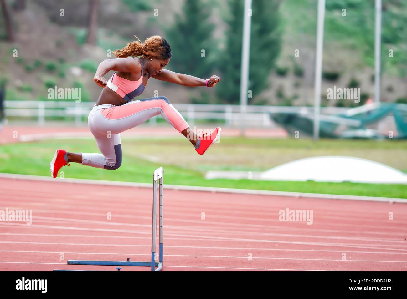 Young sportswoman jumping over hurdle during training Stock Photo
