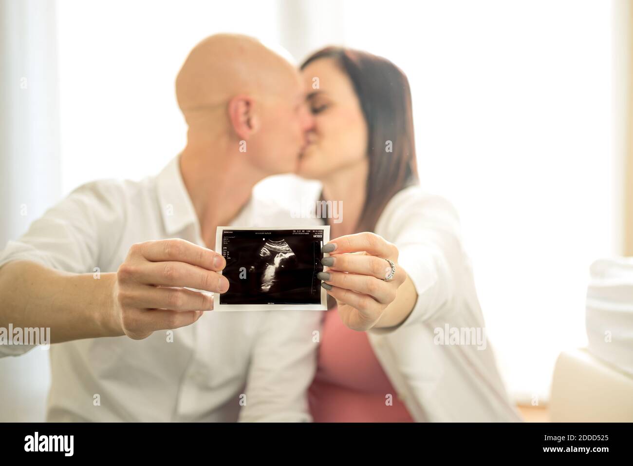 A young couple kisses happy to show the ultrasound of their baby - Husband and wife happy to have found out they are pregnant Stock Photo
