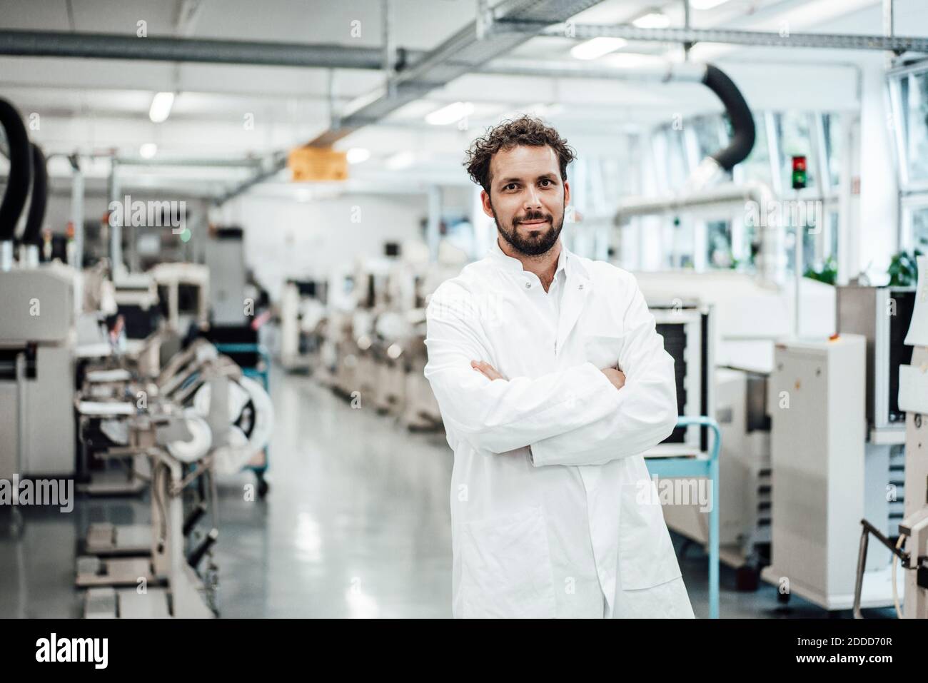 Male scientist wearing lab coat while standing with arms crossed at