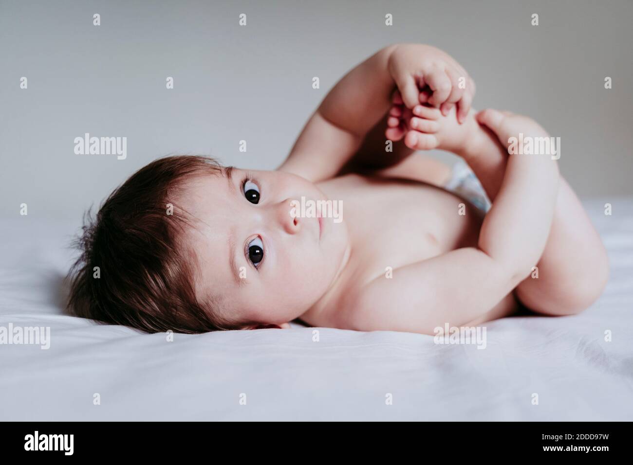 Baby boy touching legs while lying down on bed Stock Photo