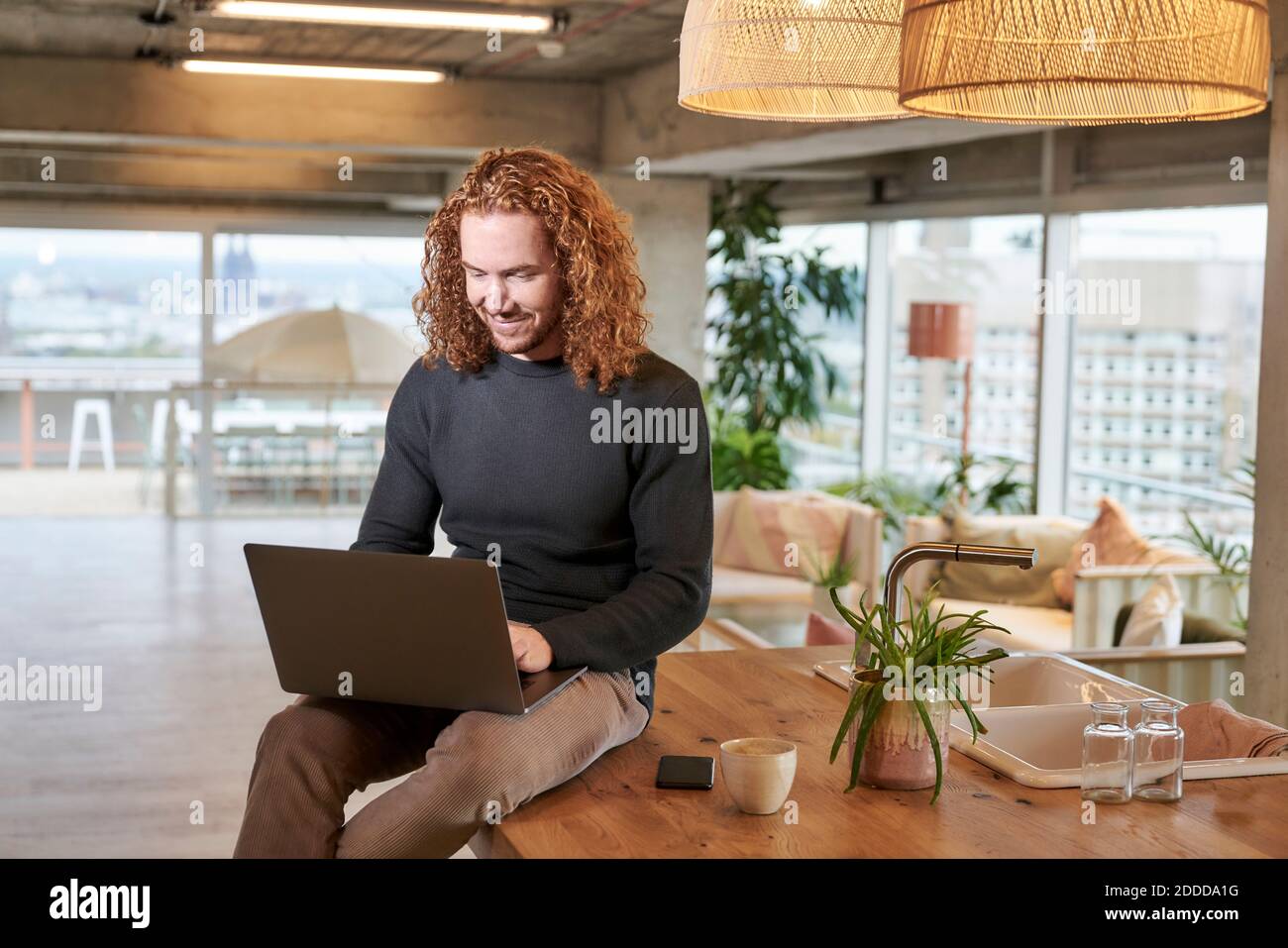 Smiling redhead man using laptop sitting on table at home Stock Photo