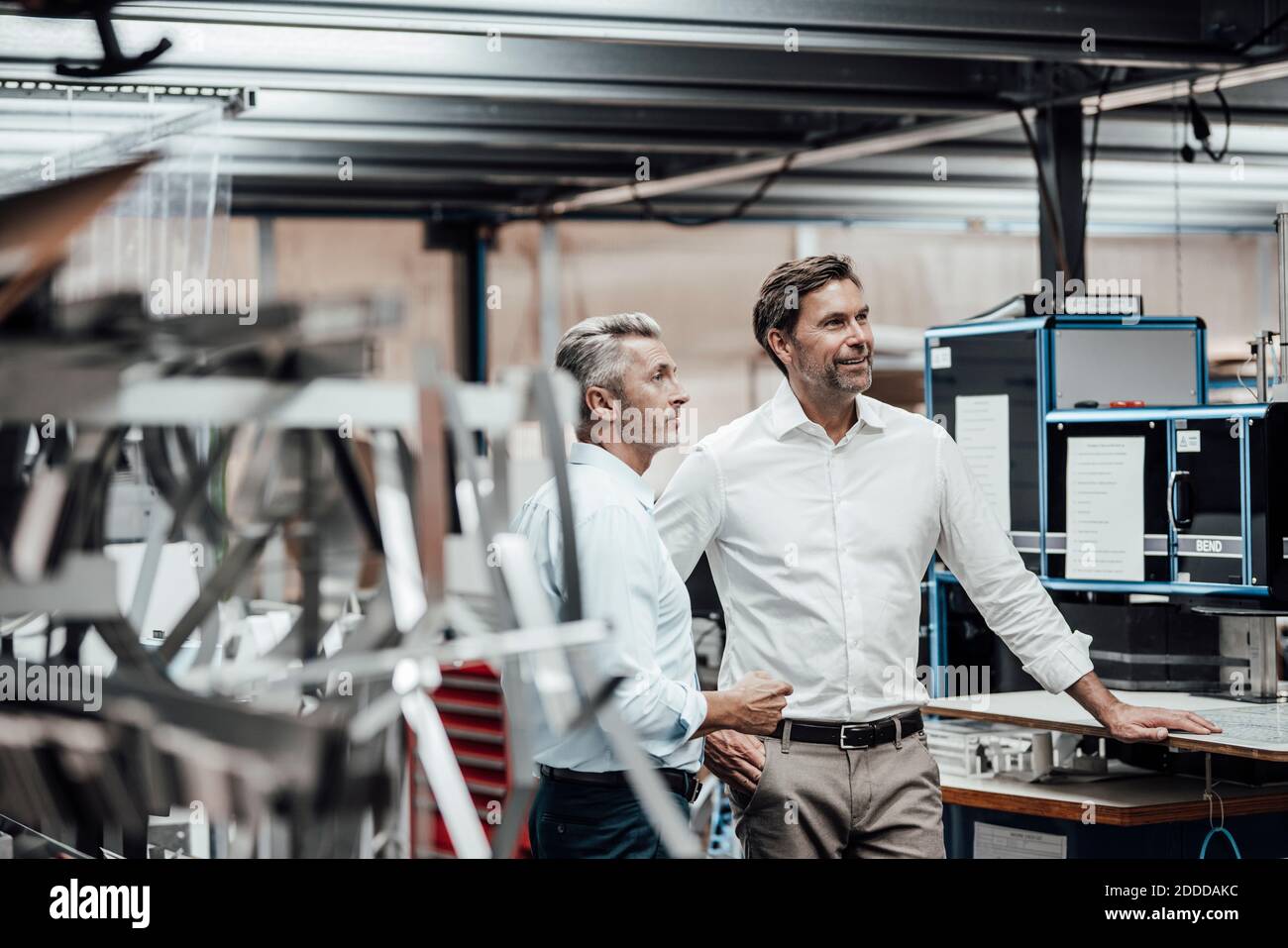 Mature colleague discussing with smiling manager while standing by manufacturing machinery in factory Stock Photo