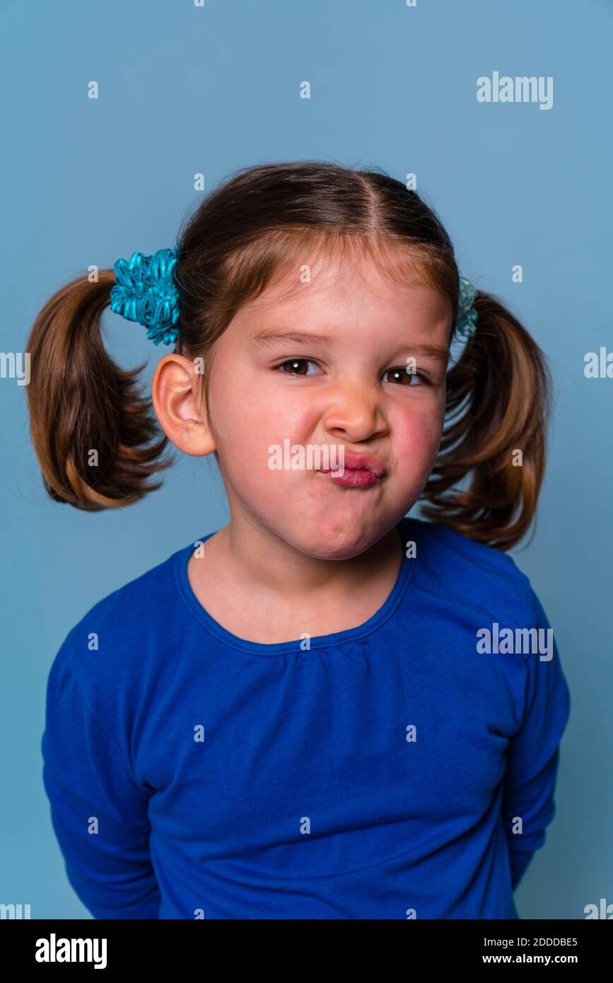 Girl making angry puckering face while standing against blue background Stock Photo