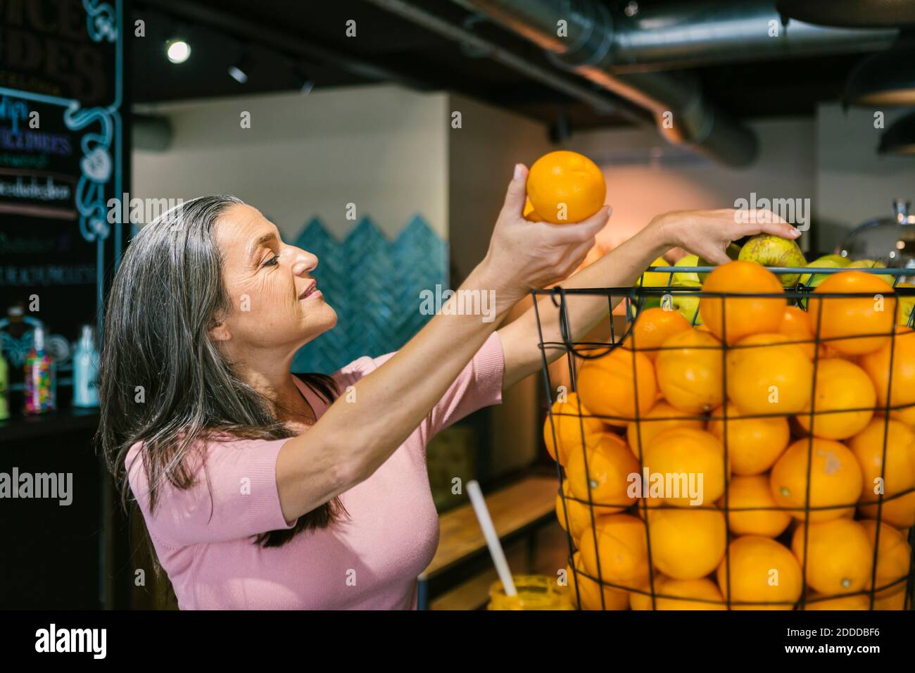 Smiling woman choosing fresh orange fruits in metallic basket at cafe Stock Photo