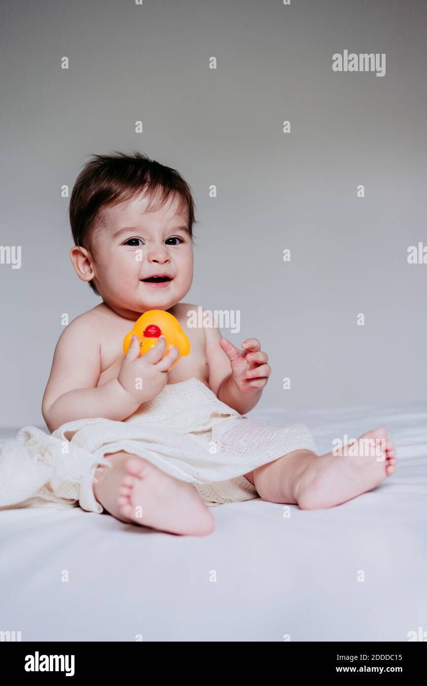 Cute boy playing with duck toy while sitting on bed at home Stock Photo ...