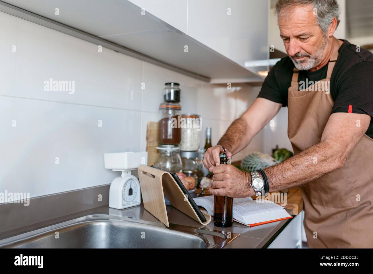 Mature man opening beer bottle while standing in kitchen Stock Photo