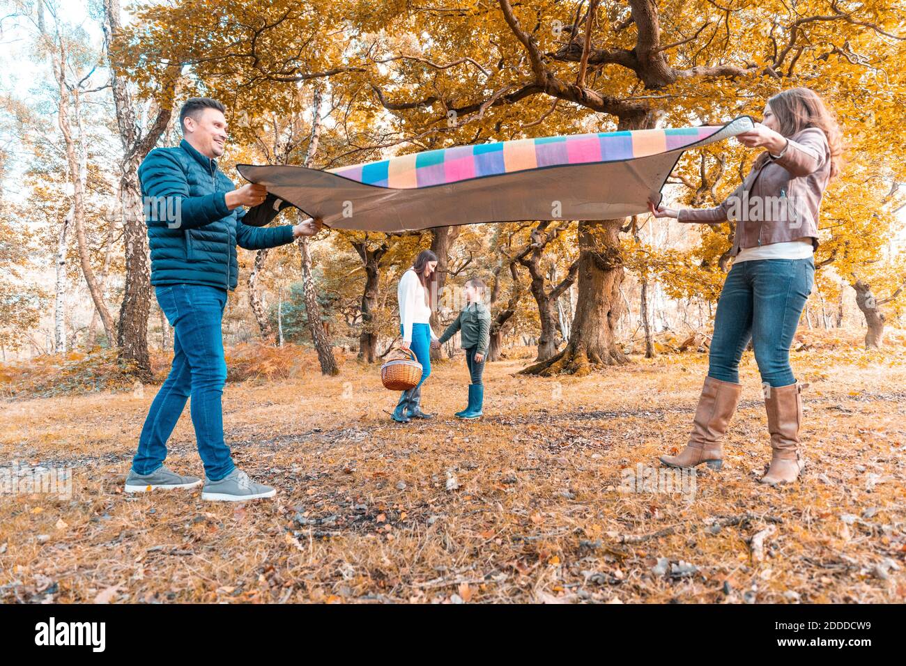 Parents laying down picnic blanket while children standing behind in