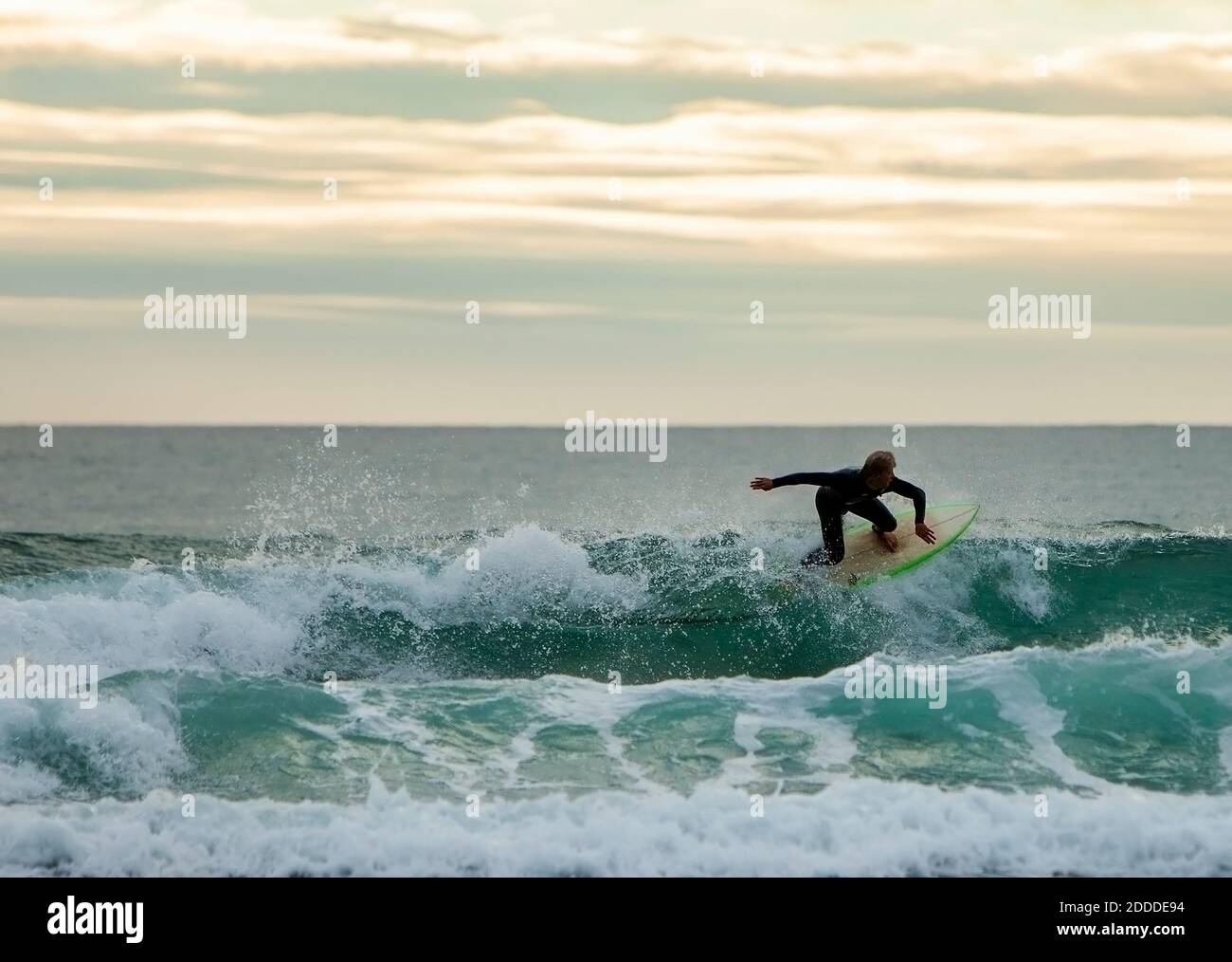 Teenage boy surfing on wave against sky during sunset Stock Photo