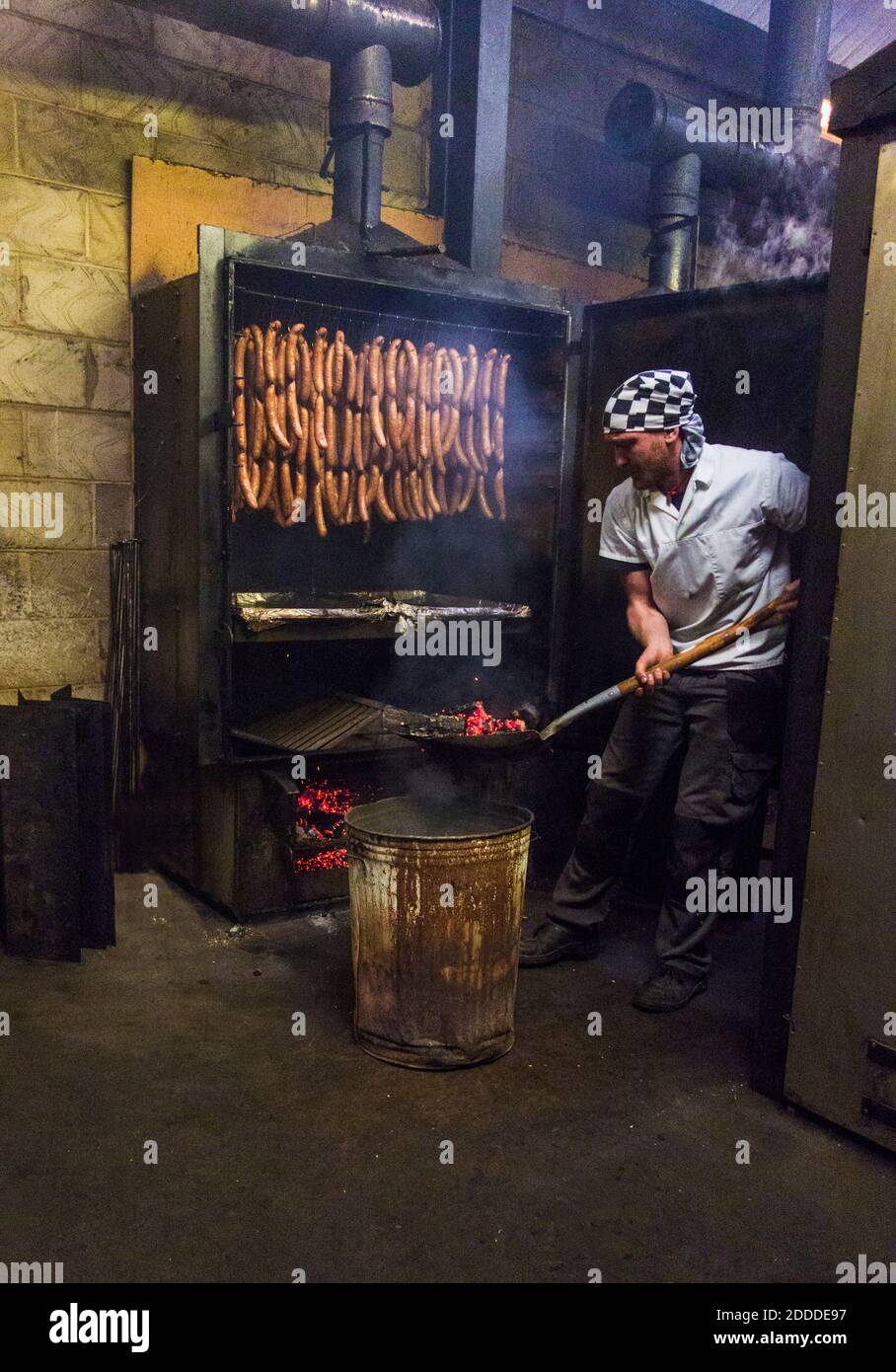 Manual worker inserting coal in smokehouse while preparing sausages at food factory Stock Photo