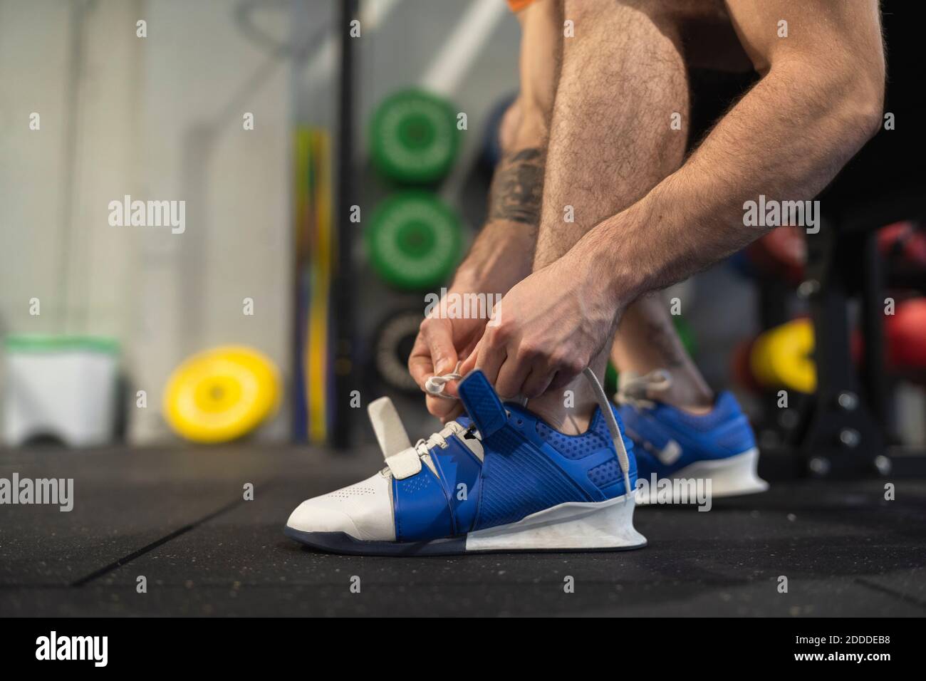 Male athlete tying shoelace while sitting in gym Stock Photo