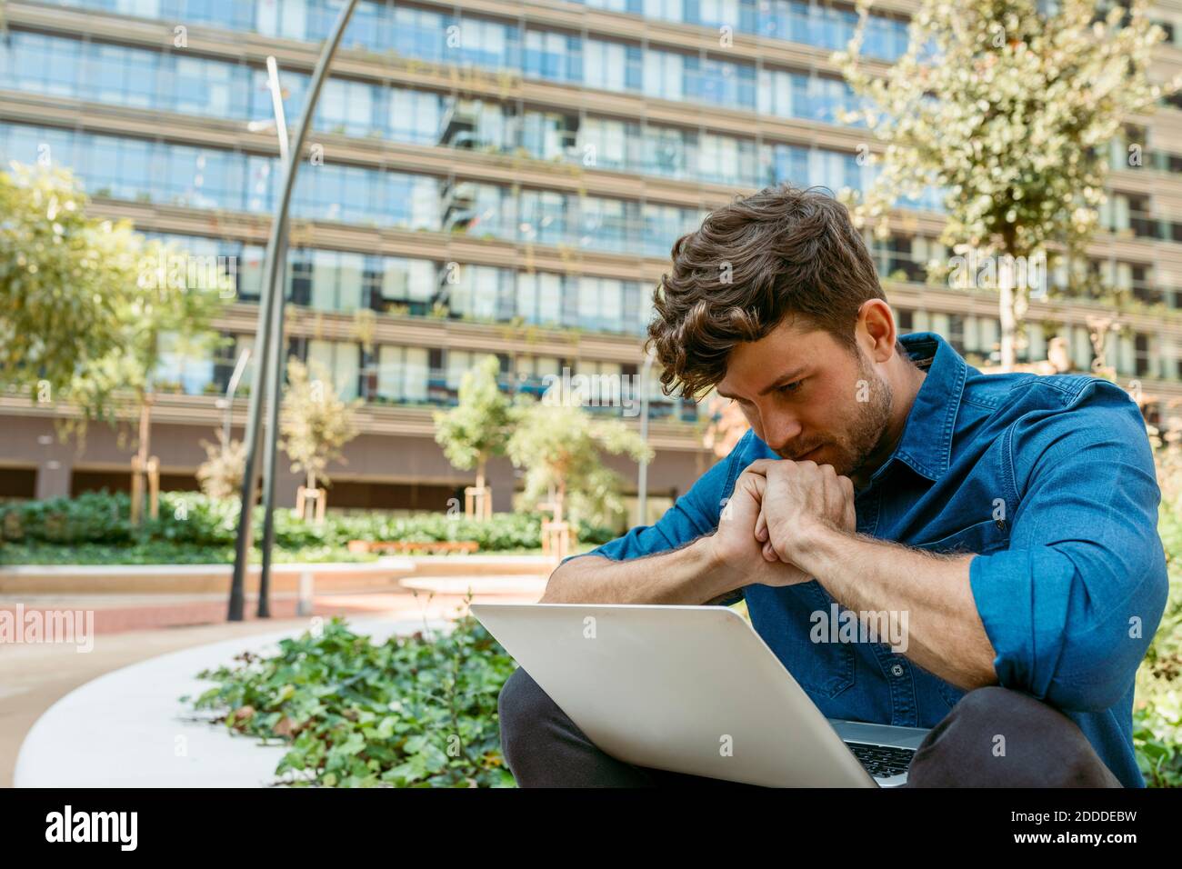 Businessman thinking while looking at laptop against office building Stock Photo