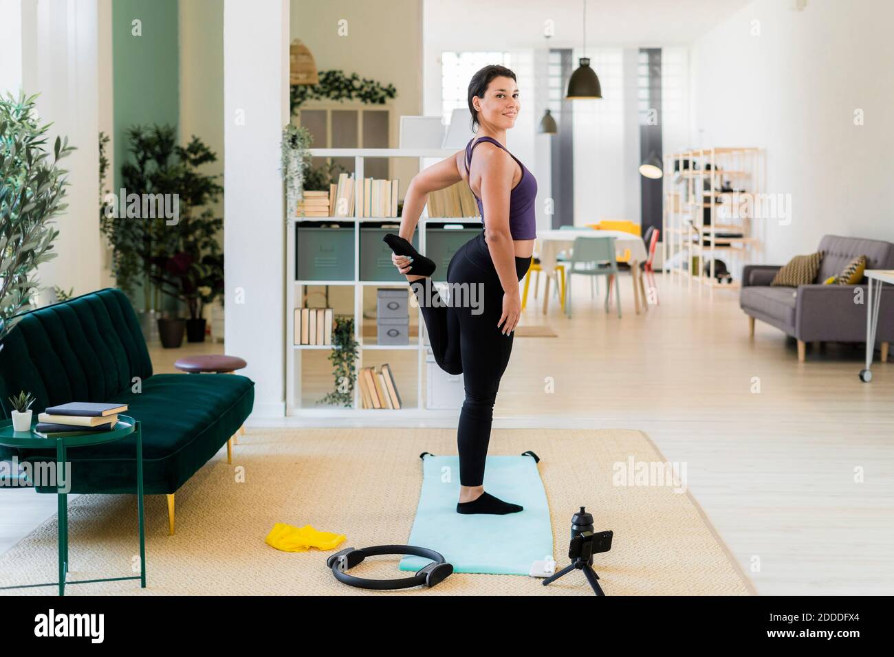 Smiling young woman standing on one leg video recording while standing at home Stock Photo