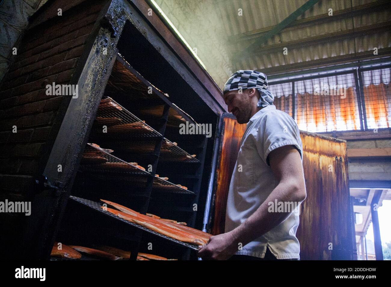 Manual worker inserting fish tray in smokehouse at food factory Stock Photo