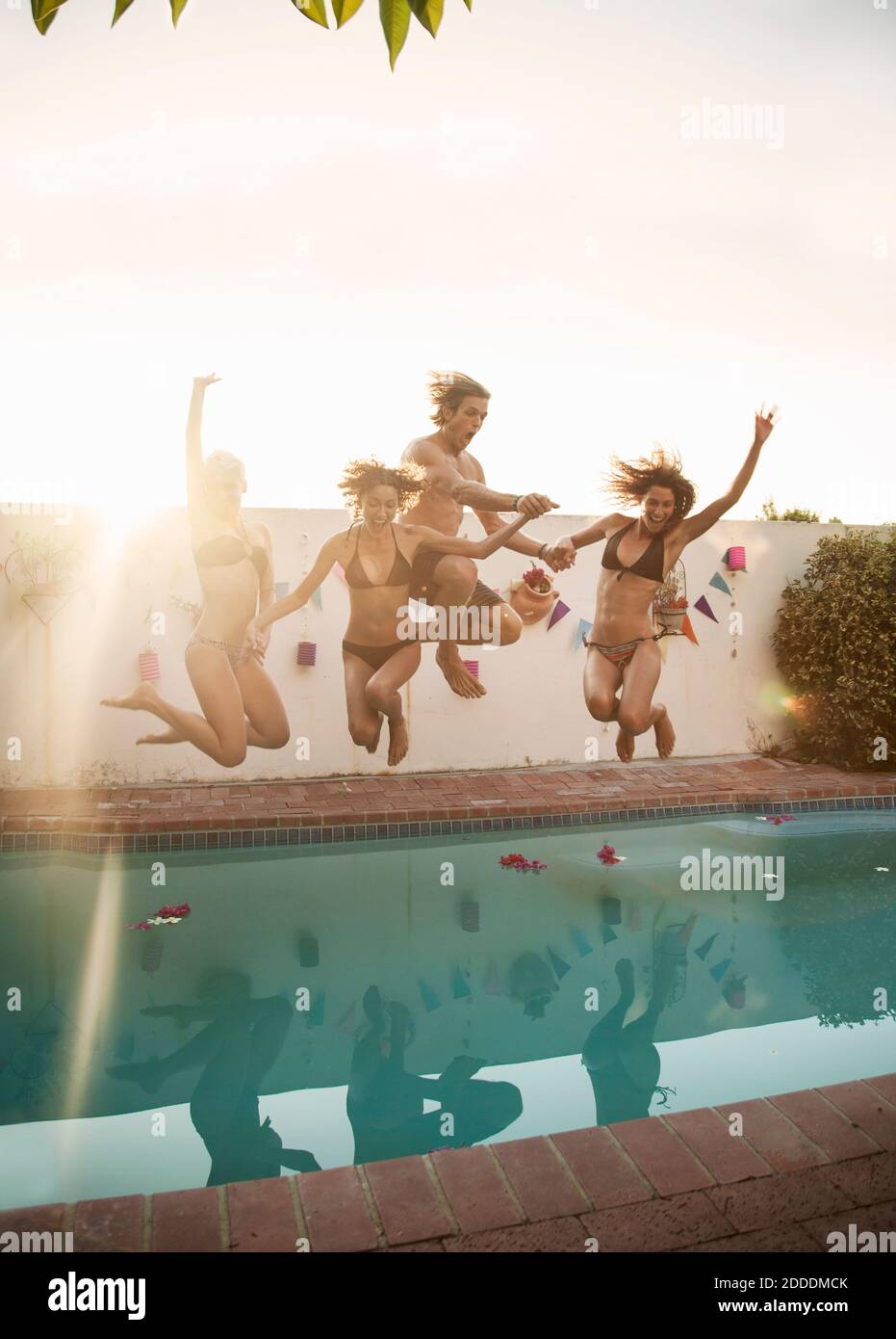 Carefree friends jumping into swimming pool against sky during sunset Stock Photo