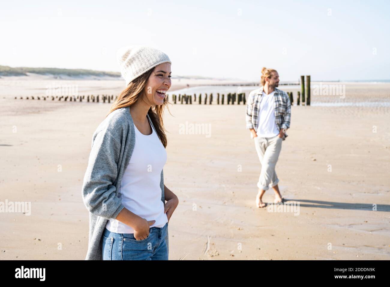 Cheerful young woman standing with hands in pockets at beach during ...