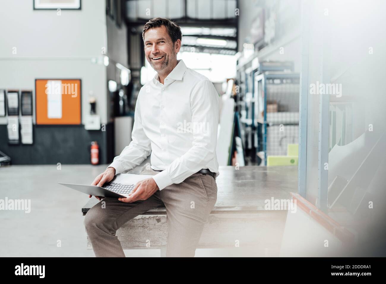 Smiling male engineer using laptop while sitting on table in industry Stock Photo