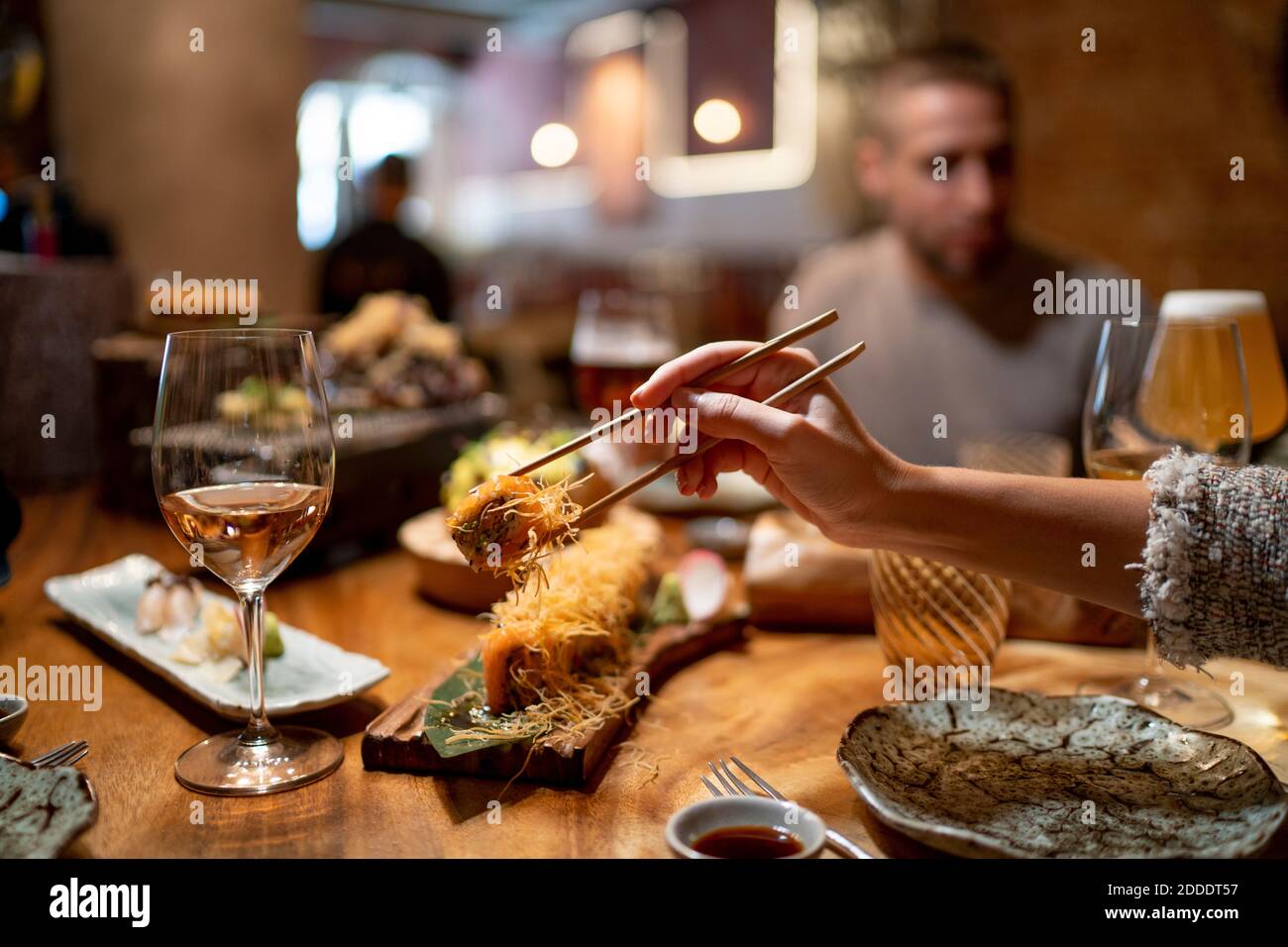 Woman using chopstick for picking up food with man sitting in background at restaurant Stock Photo
