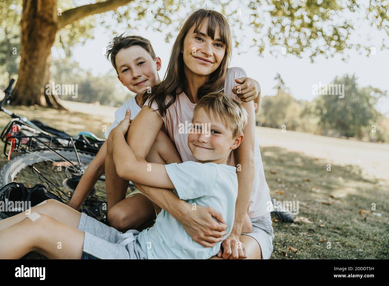 Mother embracing sons while sitting in public park Stock Photo