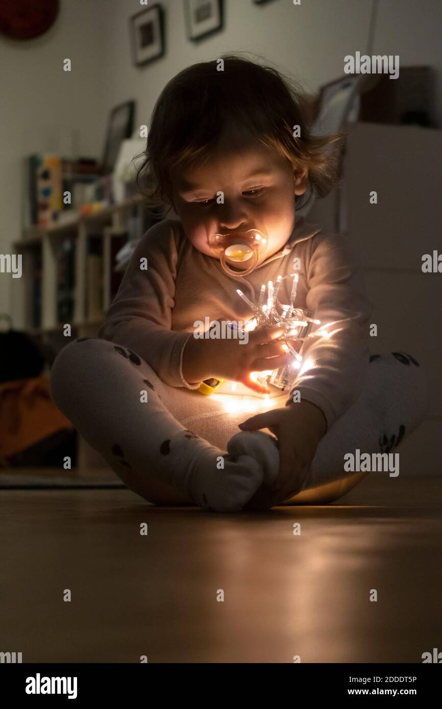 Cute baby girl holding christmas light while sitting at home Stock Photo