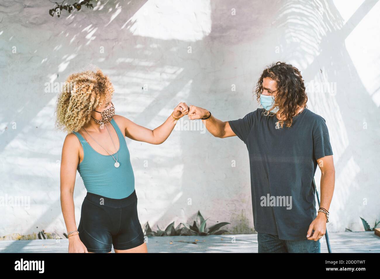 Couple with face mask giving fist bump while standing against wall Stock Photo