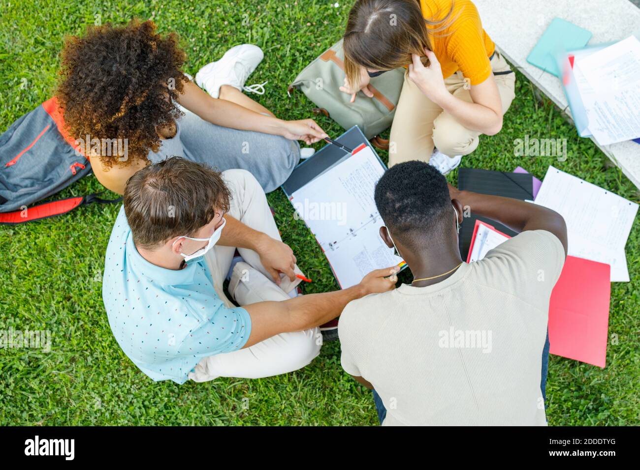 Students sitting on grass while studying together in university campus Stock Photo