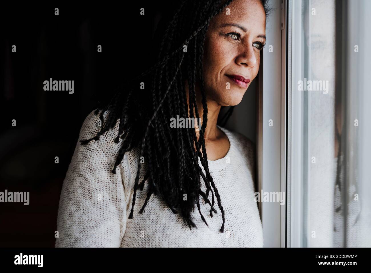Contemplating woman looking through window while standing at home Stock Photo