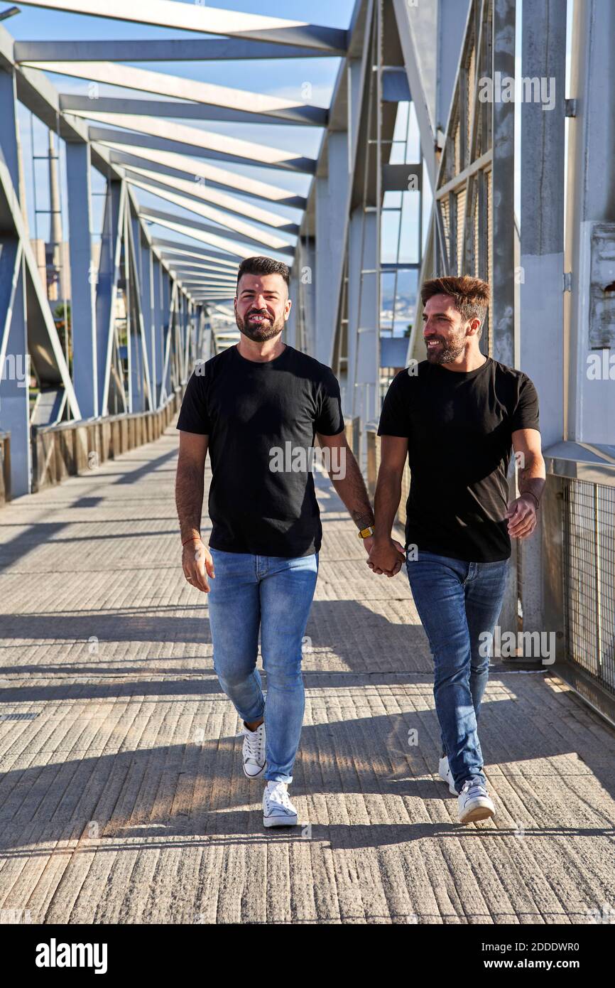 Happy homosexual couple holding hands while walking on bridge Stock Photo
