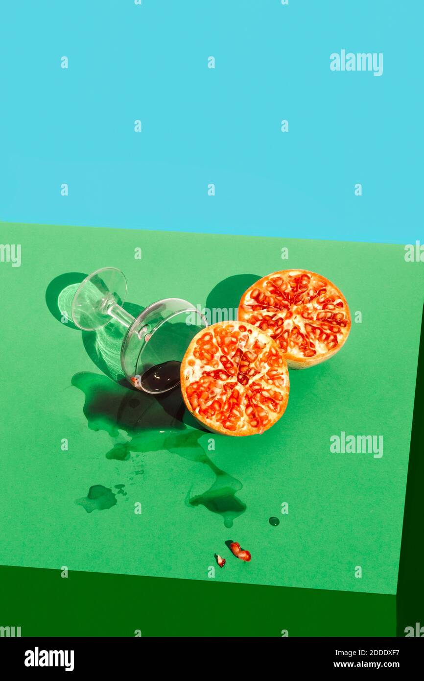 Studio shot of halved pomegranate and knocked down glass of pomegranate juice Stock Photo