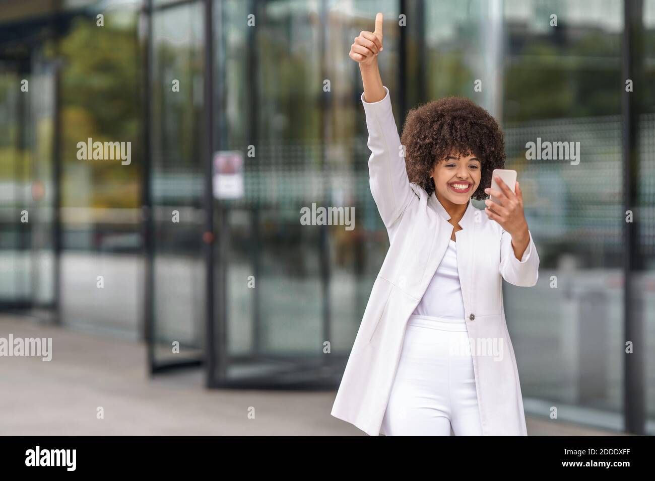 Businesswoman showing thumps up while using mobile phone outdoors Stock Photo