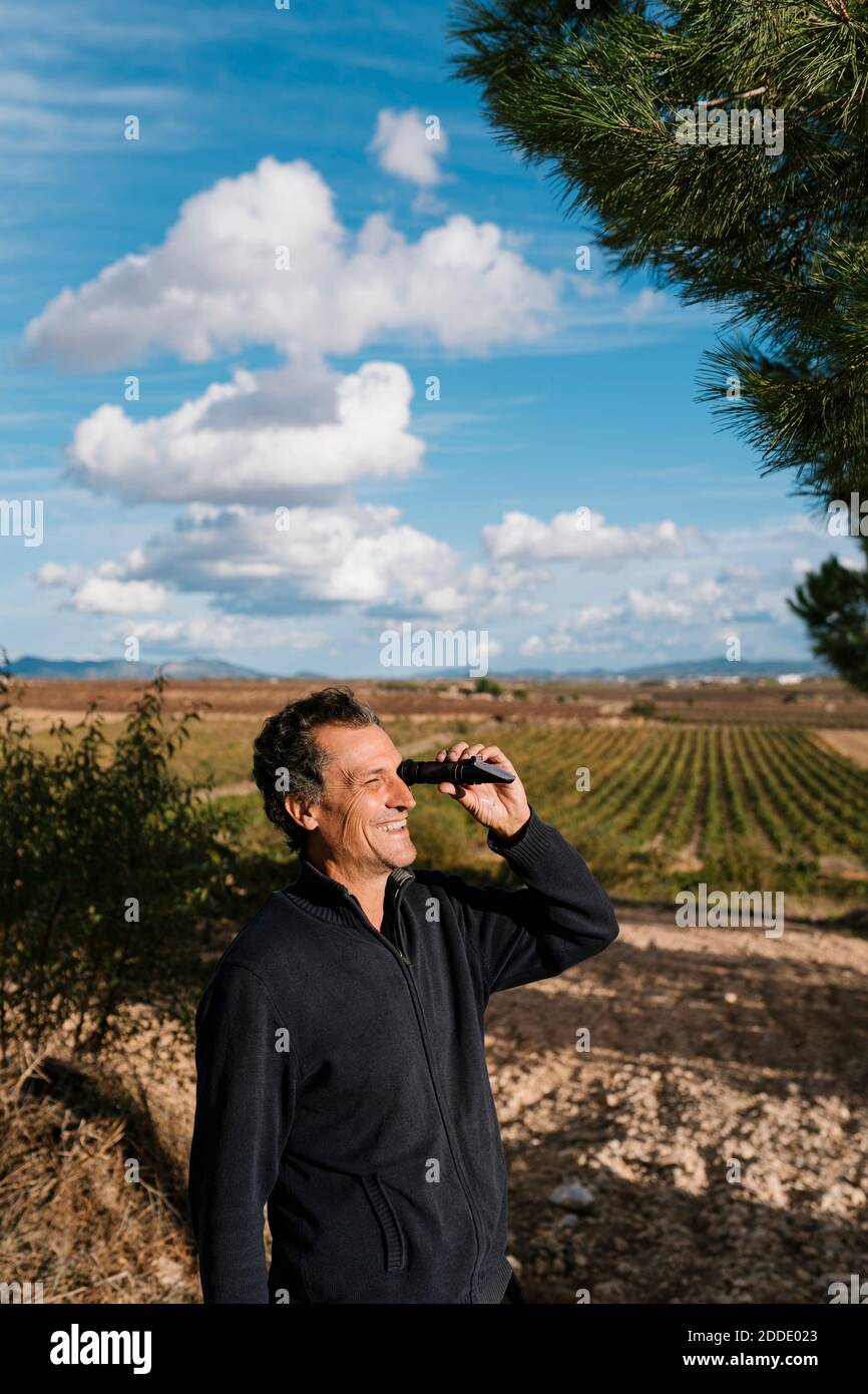 Smiling winemaker looking through refractometer at vineyard Stock Photo