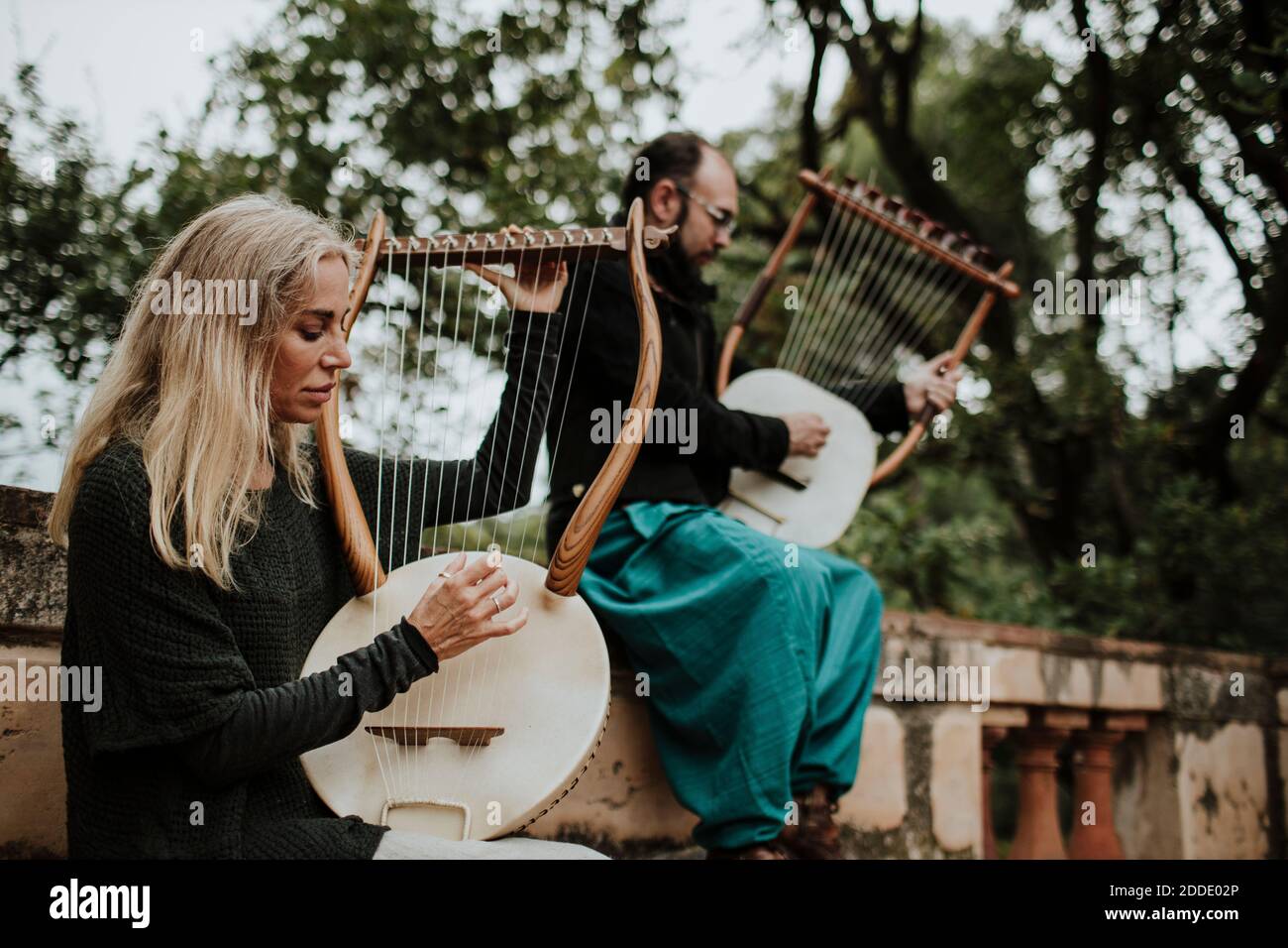 Female with male playing lyra musical instrument on bench Stock Photo