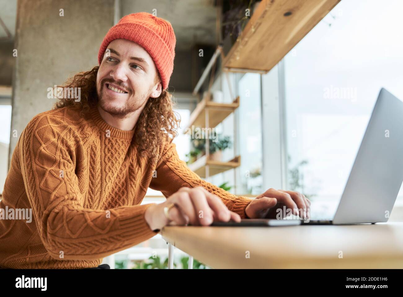 Smiling hipster man looking away while using laptop at home Stock Photo