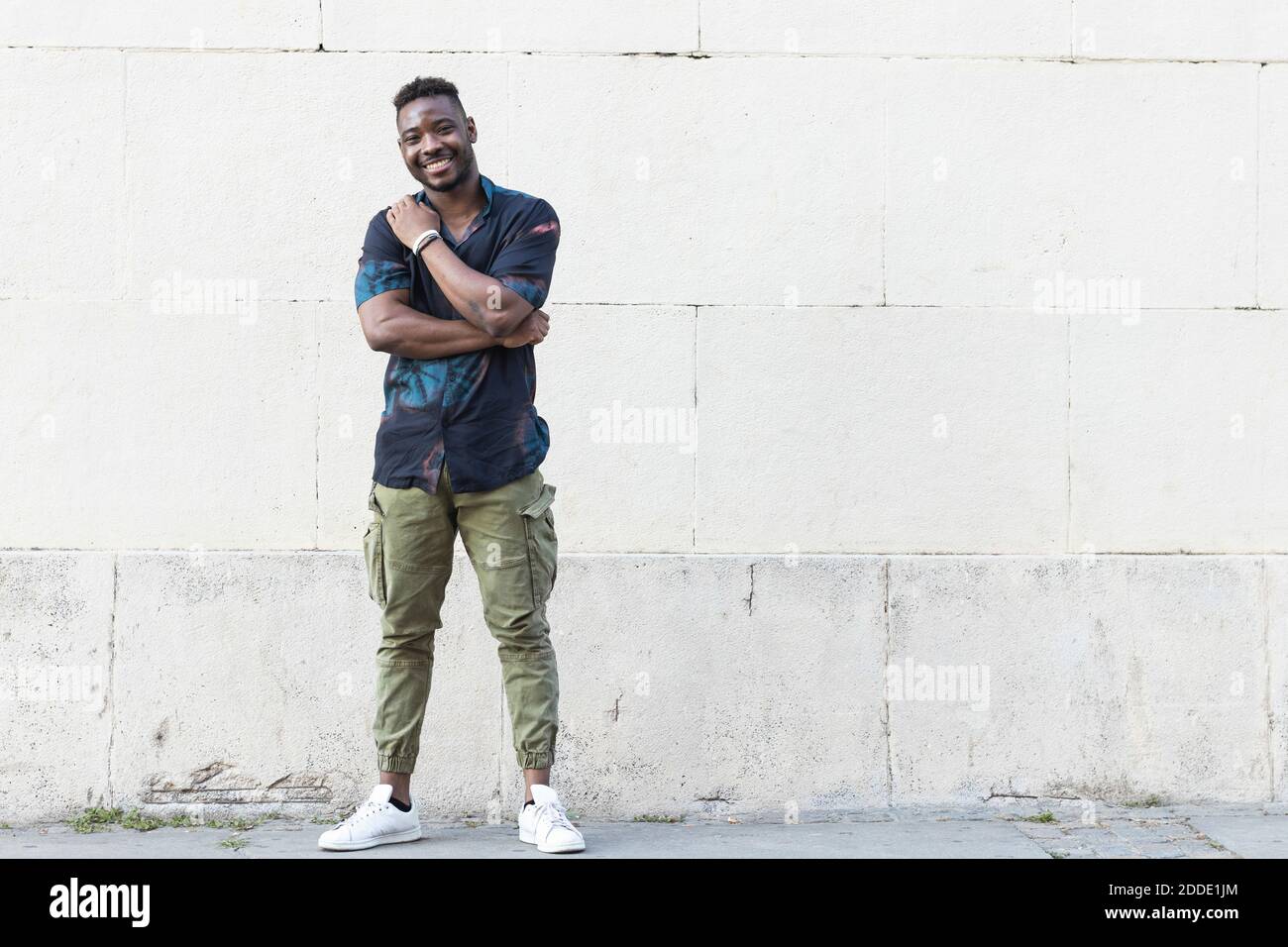 Smiling young man in casuals standing against white wall Stock Photo ...