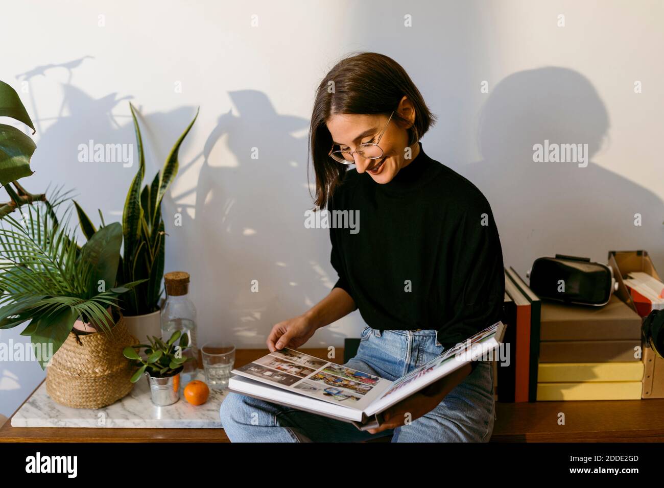 Smiling woman looking photographs in photo album while sitting at home Stock Photo