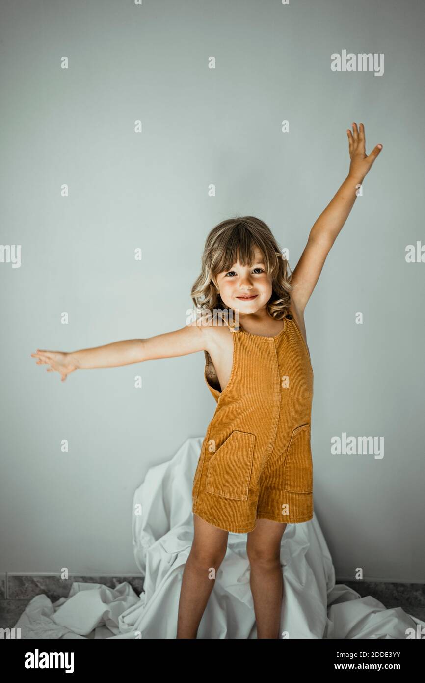 Cute girl with arms outstretched standing against wall at home Stock Photo