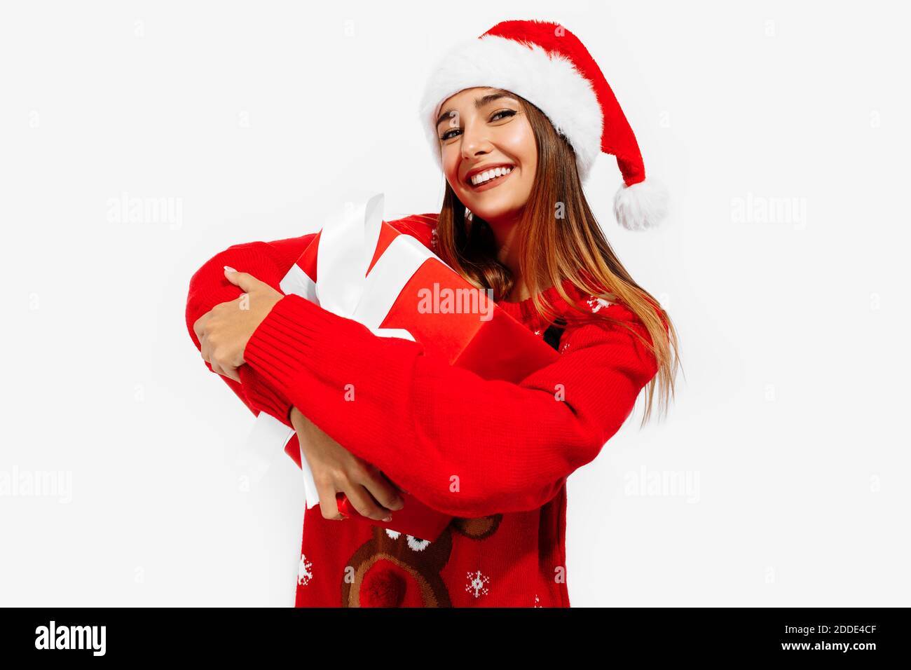 Happy cute young woman in christmas sweater and santa claus hat hugging ...