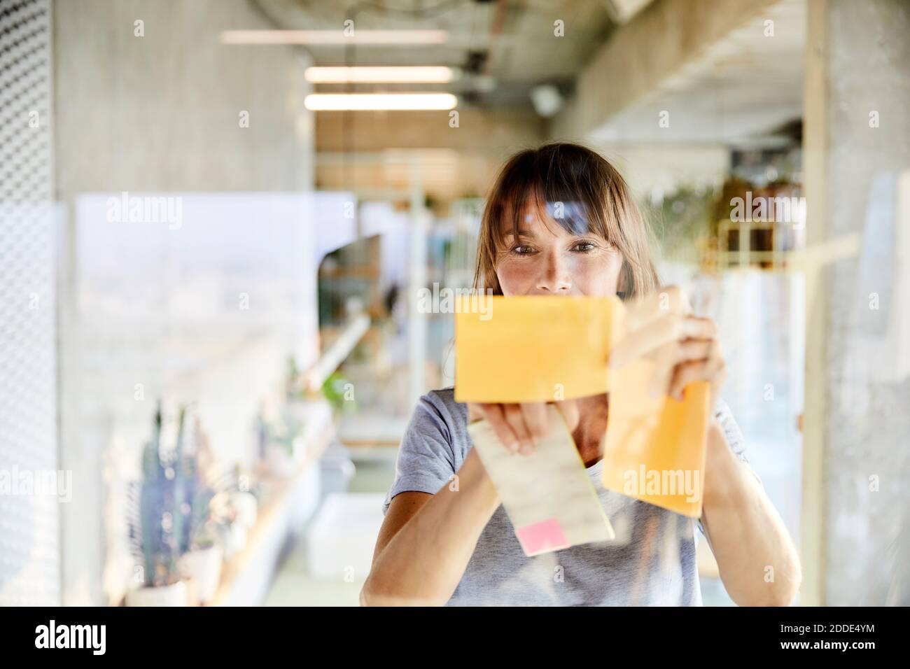 Mature woman sticking sticky notes on glass material Stock Photo