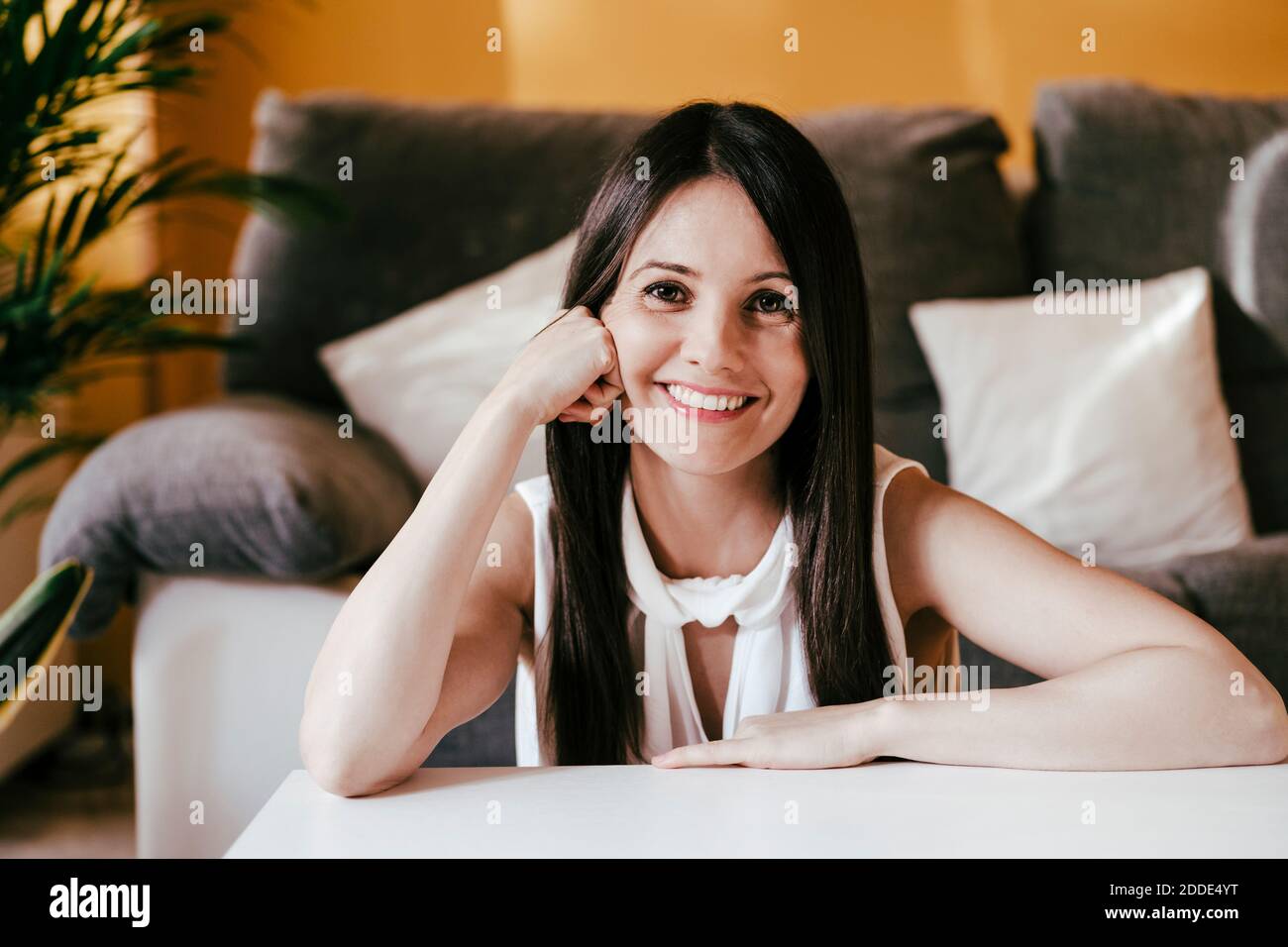 Smiling woman with hand on chin sitting at home Stock Photo - Alamy