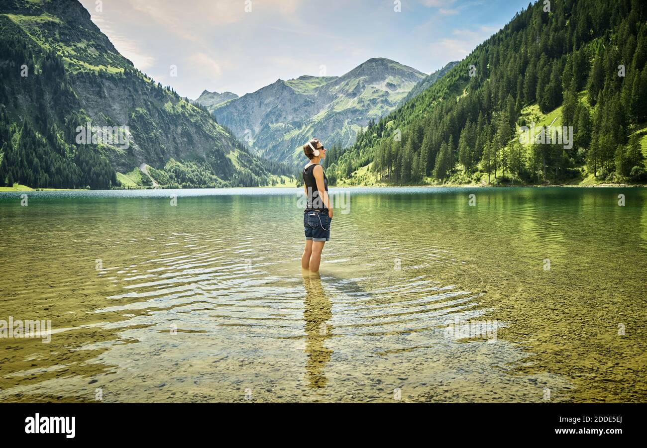 Mature woman standing knee deep in Vilsalpsee while listening music on sunny day Stock Photo