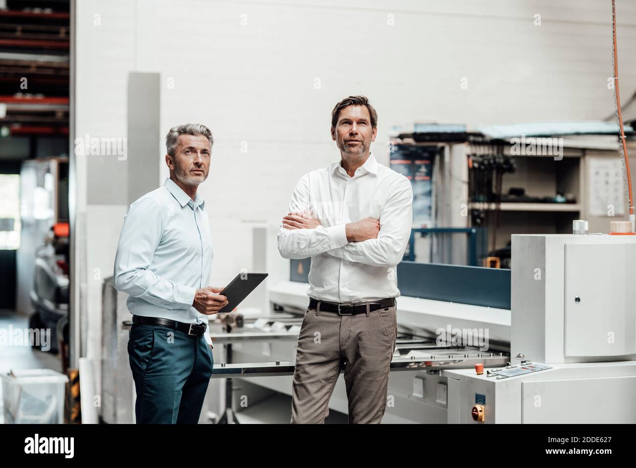 Male engineers looking away while standing by machinery in factory Stock Photo