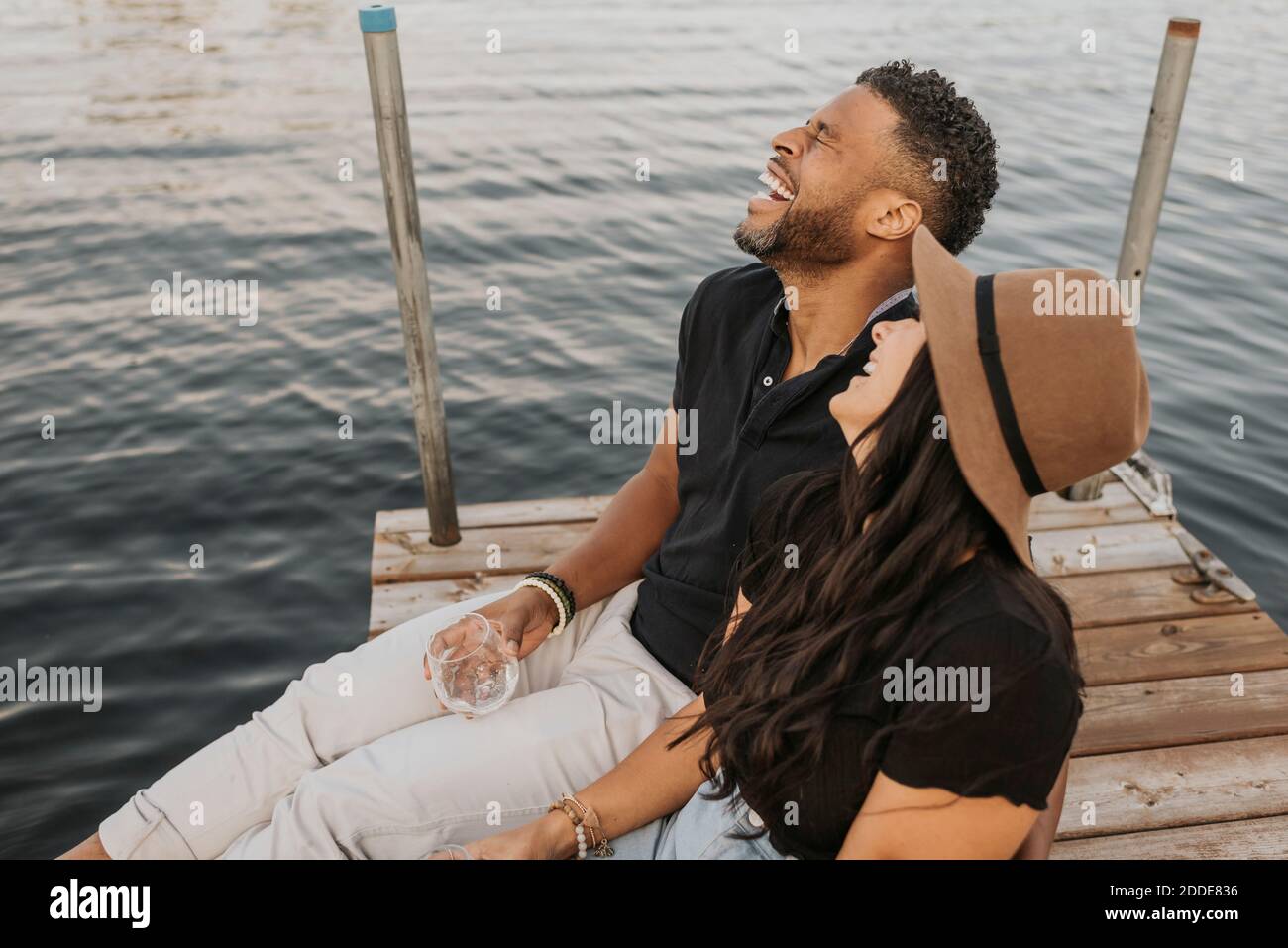 Happy couple drinking wine while sitting on pier Stock Photo