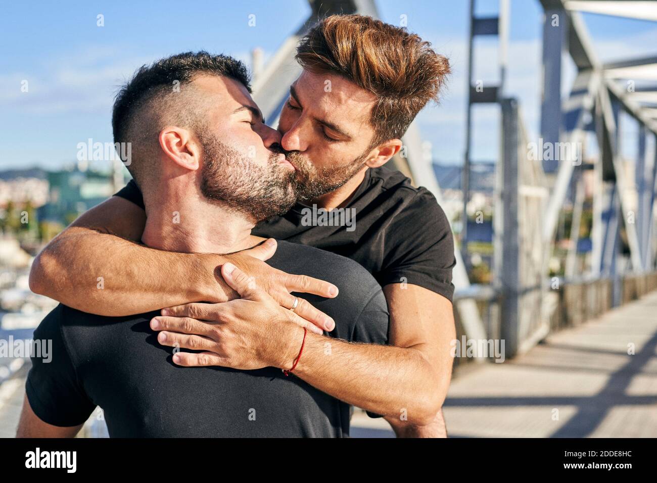 Gay man kissing boyfriend on footbridge during sunny day Stock Photo